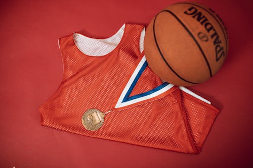 Foto de stock de una medalla de bronce en una camiseta roja al lado de un balón de baloncesto sobre una superficie roja