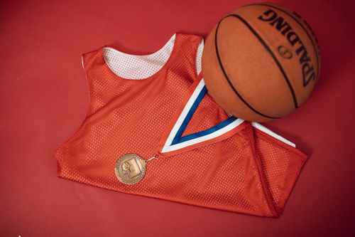 Free A red basketball jersey paired with a medal and Spalding basketball on a red backdrop. Stock Photo