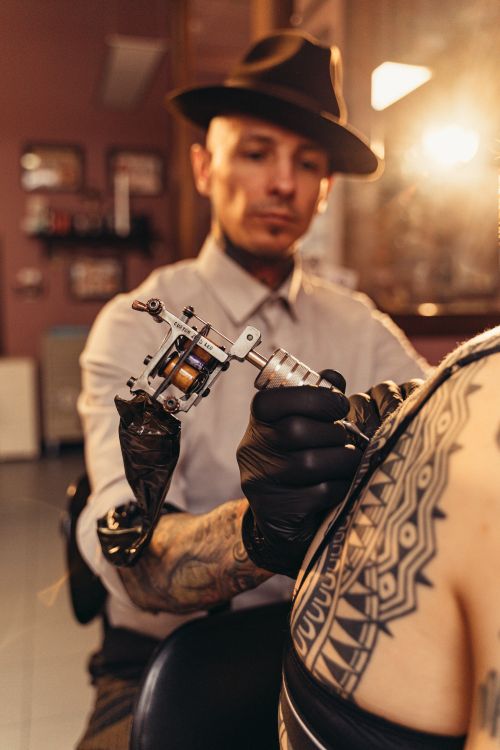 A tattoo artist using a machine to apply a detailed geometric design on a client's arm in a studio setting