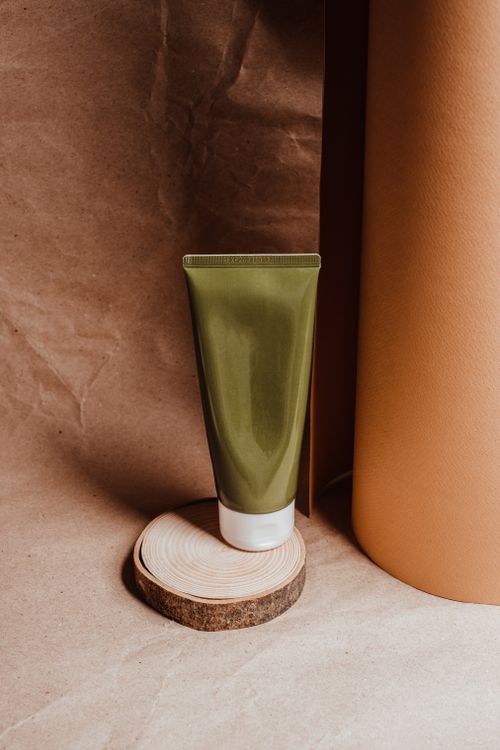Free A simple and elegant green cosmetic tube displayed on a wooden stand against a brown paper background. Stock Photo