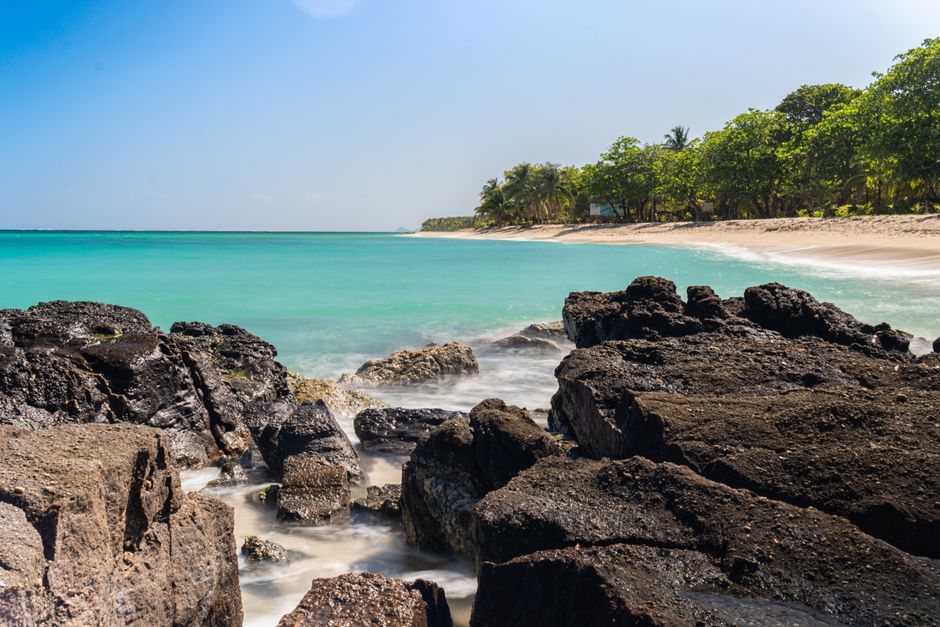 Tropical beach with dark volcanic rocks and clear turquoise water