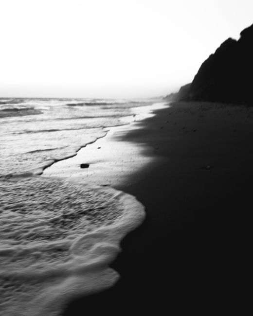 Black and white photo of waves on a quiet seashore at dawn.
