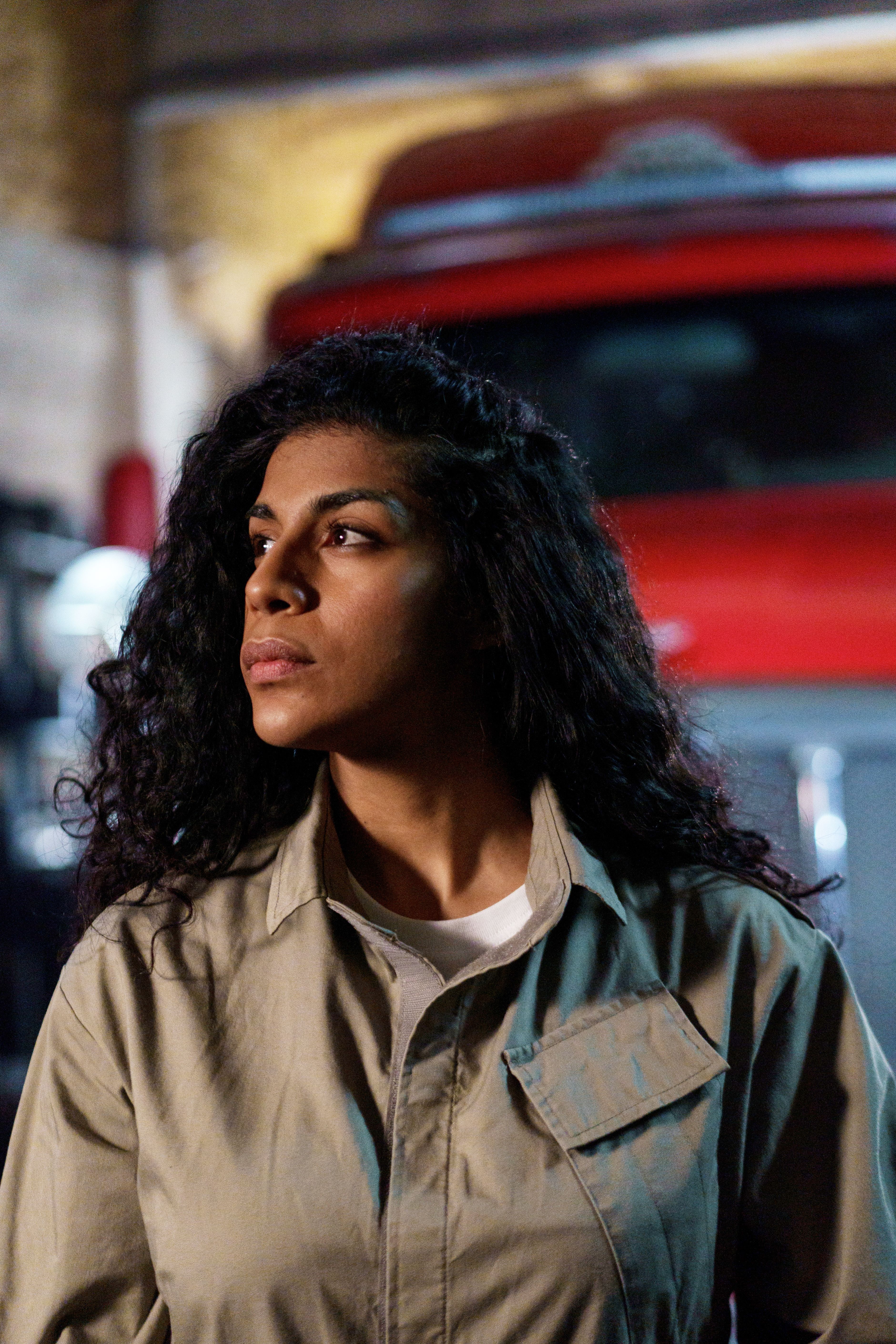 Portrait of a woman mechanic with curly hair in uniform, looking thoughtfully away.