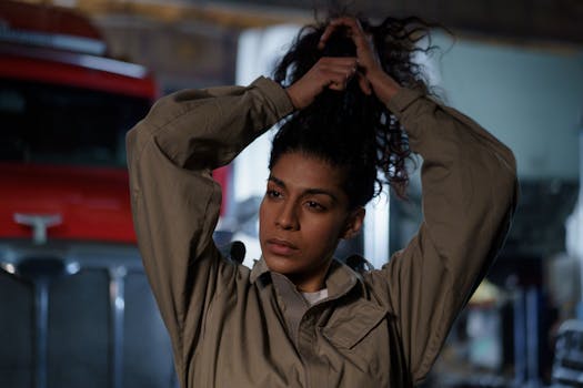 Woman in beige uniform tying her hair in front of a fire truck, exuding confidence.