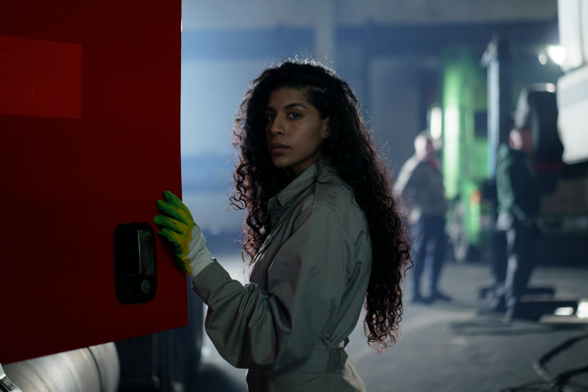 A confident female mechanic in coveralls working on trucks inside a garage.