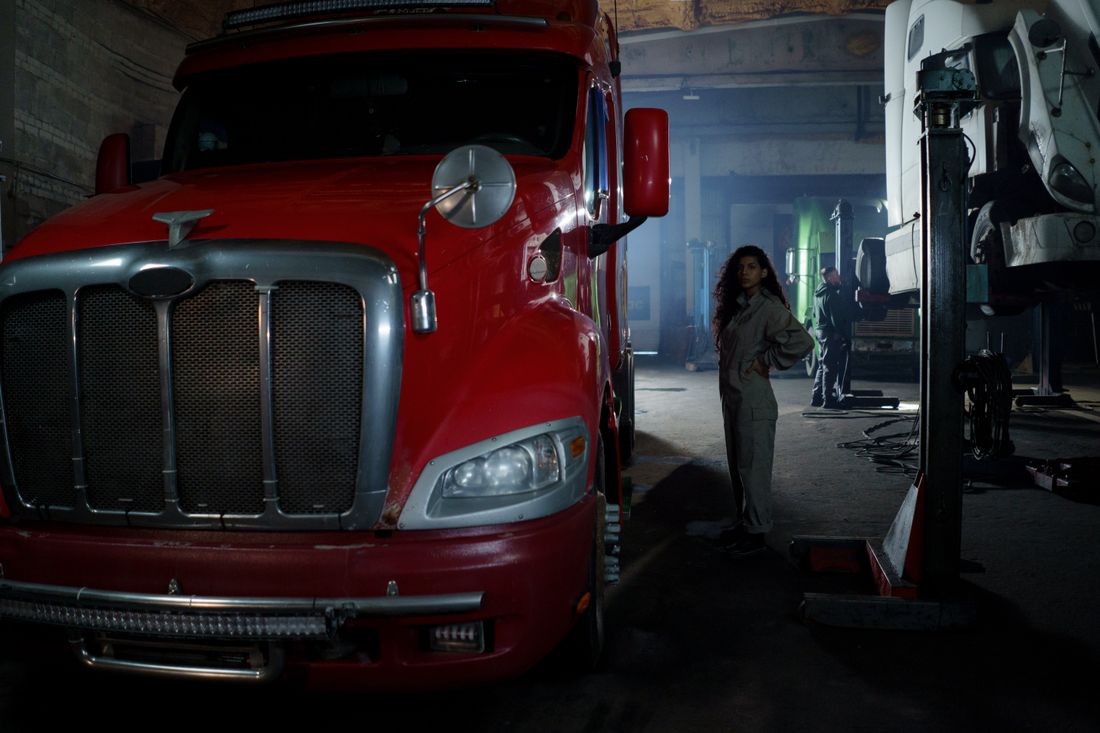 Female mechanic with curly hair stands confidently next to a red truck