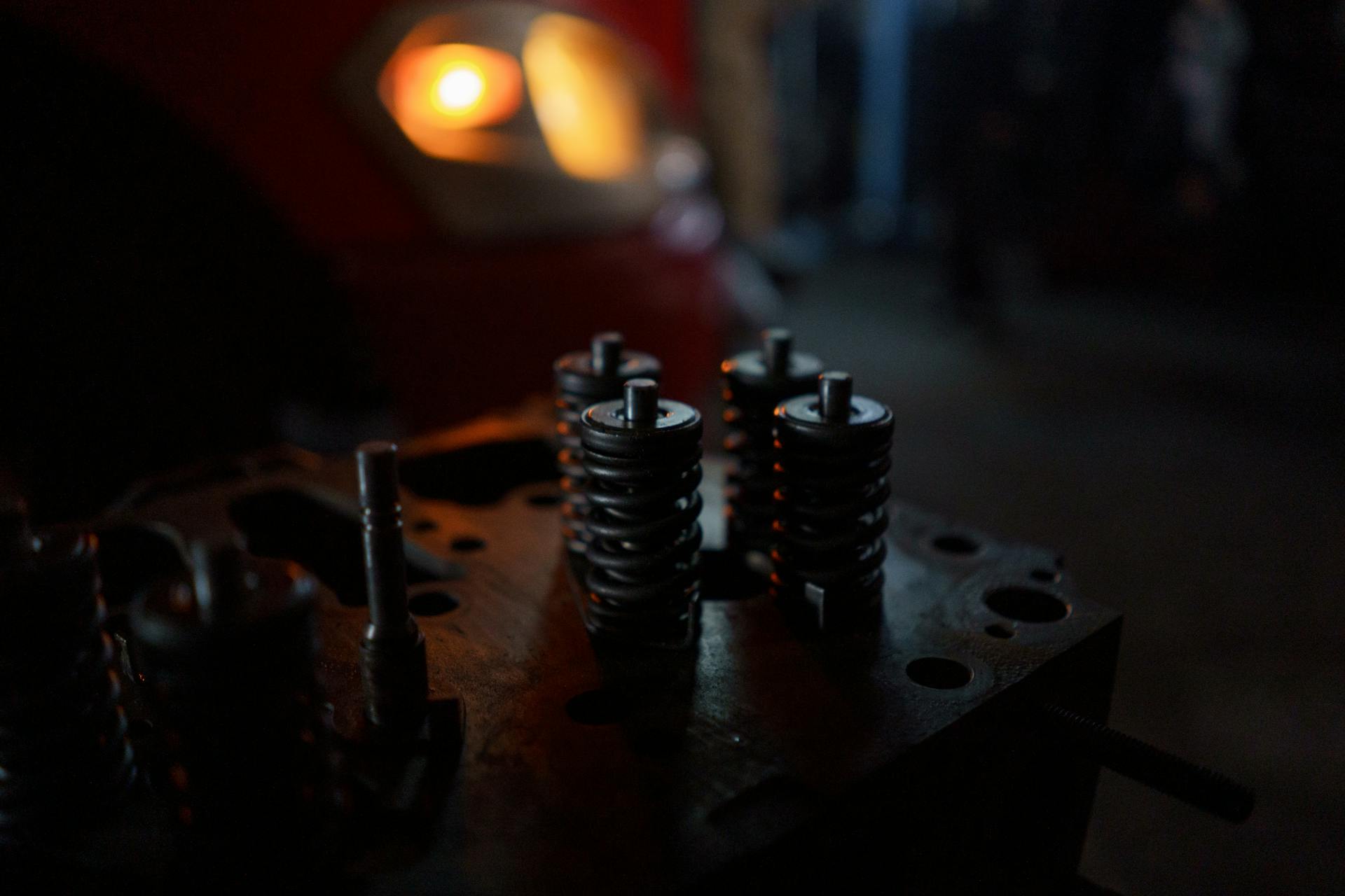 Detailed view of engine valve springs on a cylinder head with a blurred background in a workshop.