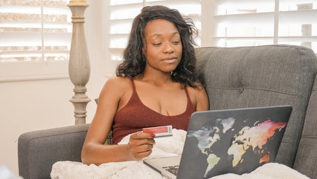 Young woman using her credit card for an online purchase while sitting on a couch with a laptop at home.