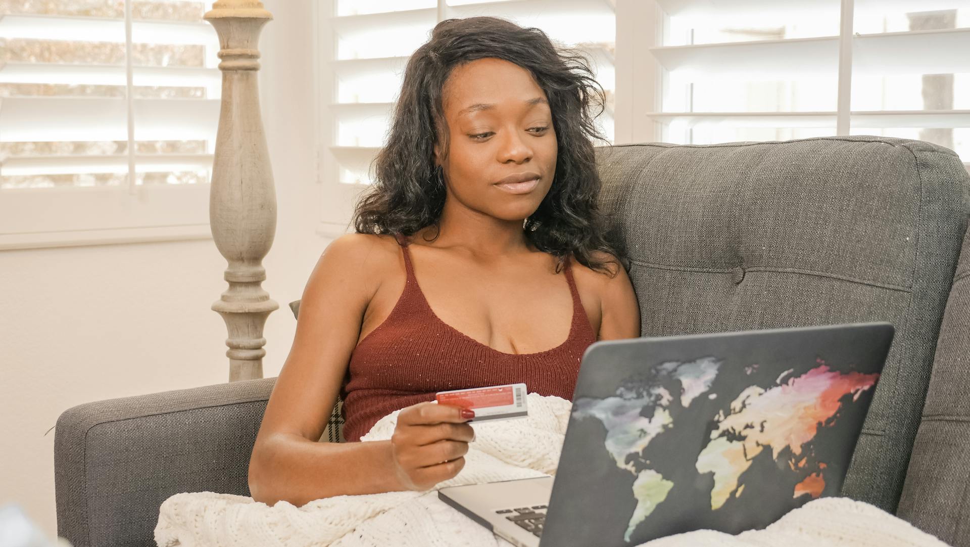 Young woman using her credit card for an online purchase while sitting on a couch with a laptop at home.