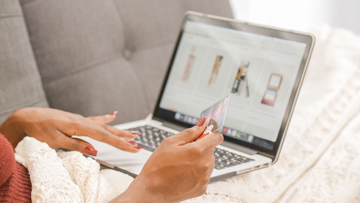Mulher deitada no sofá fazendo compras online no notebook com um cartão de crédito na mão