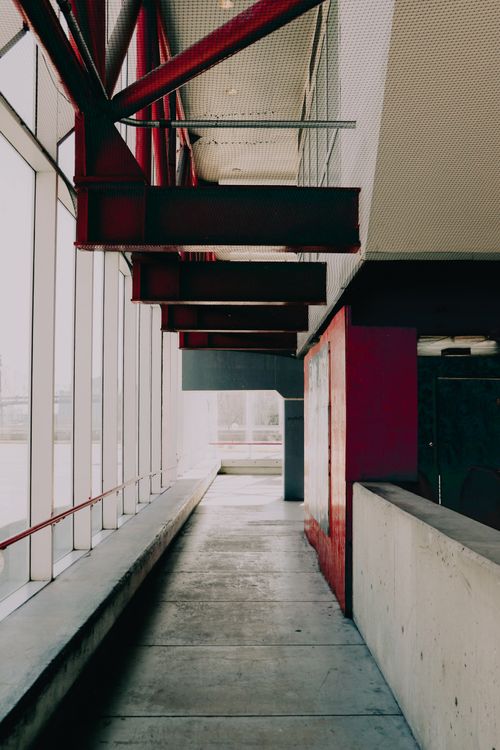 Free Vertical shot of a modern indoor walkway with concrete elements and large glass windows, showcasing architectural design. Stock Photo