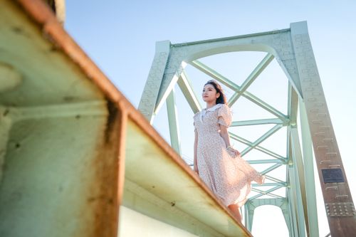 Free A young woman in a floral dress poses gracefully on a bridge under clear daylight. Stock Photo