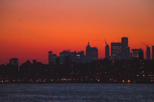 Free Silhouette of the New York City skyline during a vibrant sunset over the river. Stock Photo