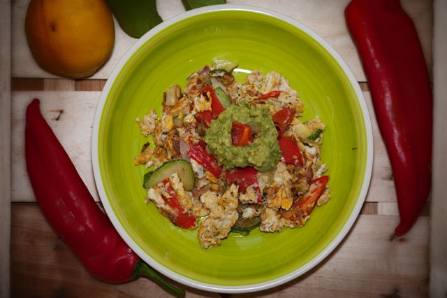 Vibrant egg and vegetable dish garnished with guacamole and surrounded by fresh peppers.