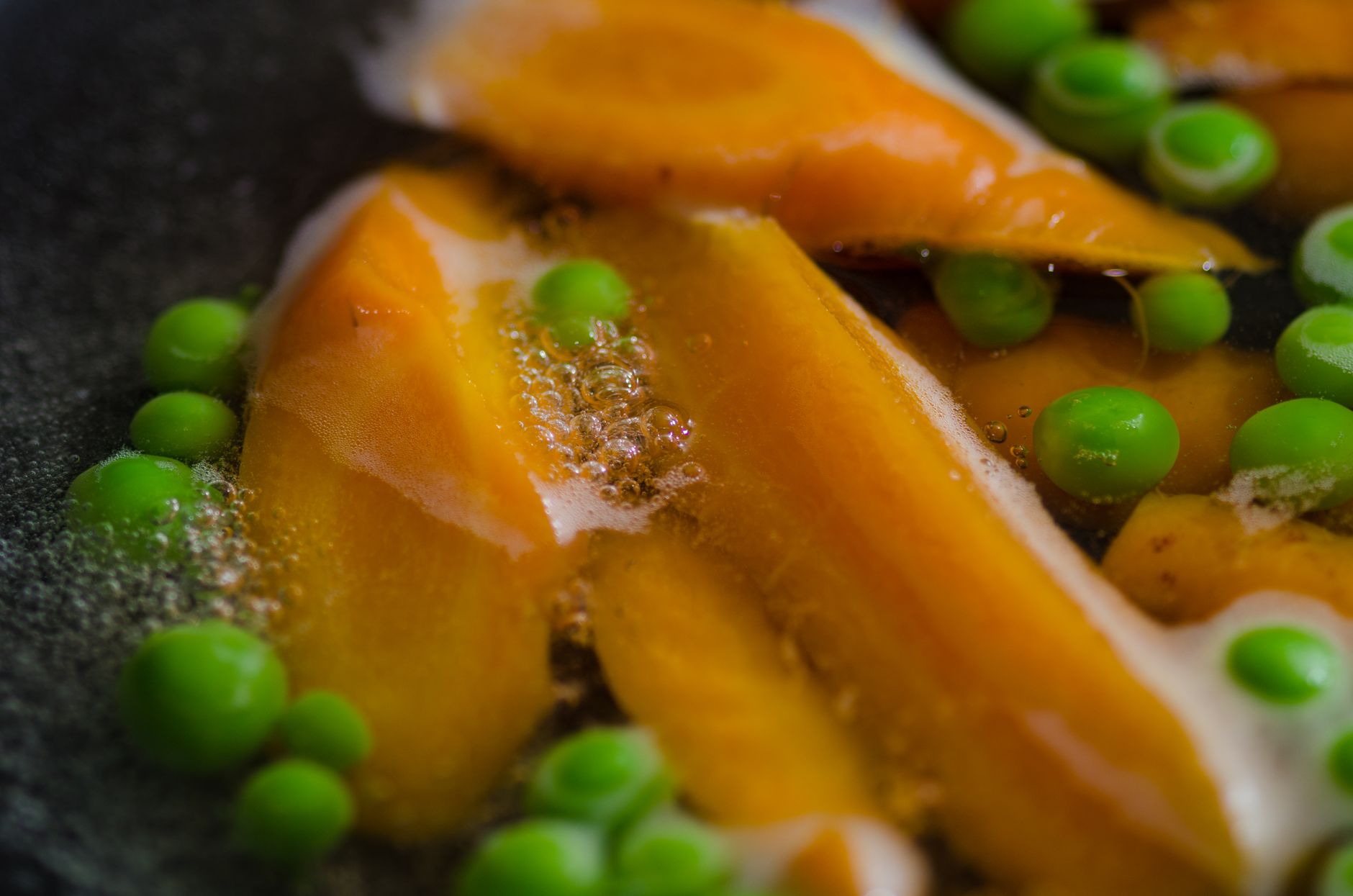 Close-up of carrots and peas boiling with bubbles in hot water, showcasing fresh vegetables.