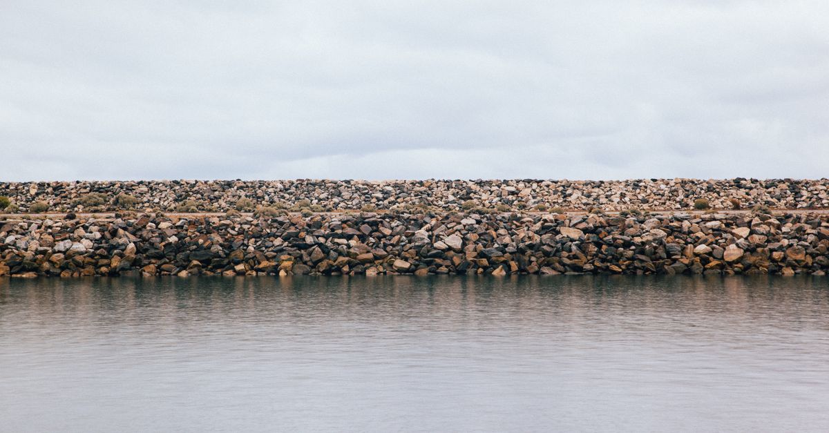 A tranquil view of a rock barrier by the ocean under a cloudy sky, creating a serene atmosphere.