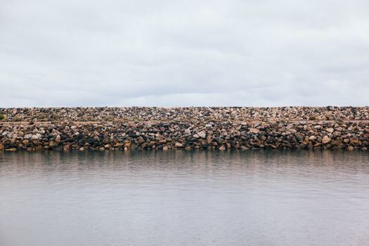 A tranquil view of a rock barrier by the ocean under a cloudy sky, creating a serene atmosphere.