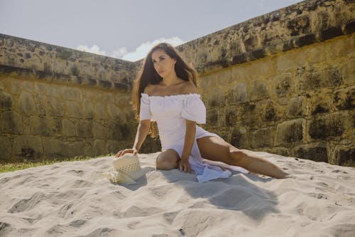 A Woman in White Off Shoulder Dress Sitting on Sand