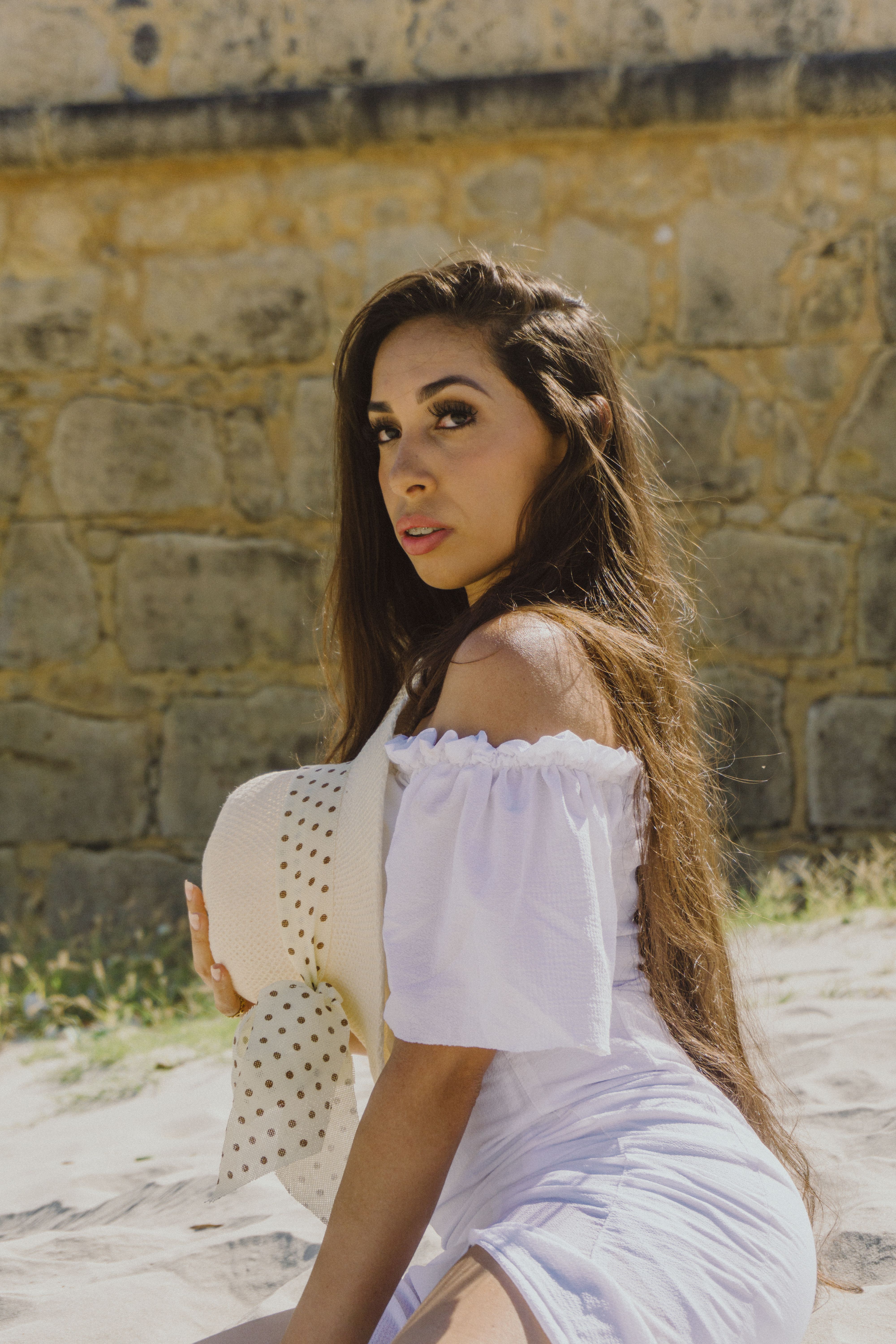 Portrait of a stylish woman with long hair in a summer dress holding a hat outdoors.