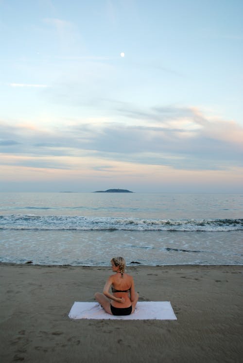 Anonymous lady in swimwear relaxing on sandy seashore at sundown