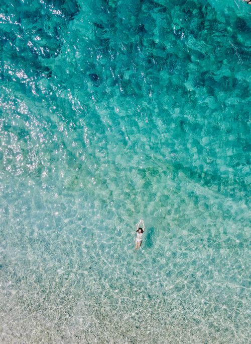 Free Aerial shot of a woman swimming in the clear turquoise sea, showcasing serene coastal beauty. Stock Photo