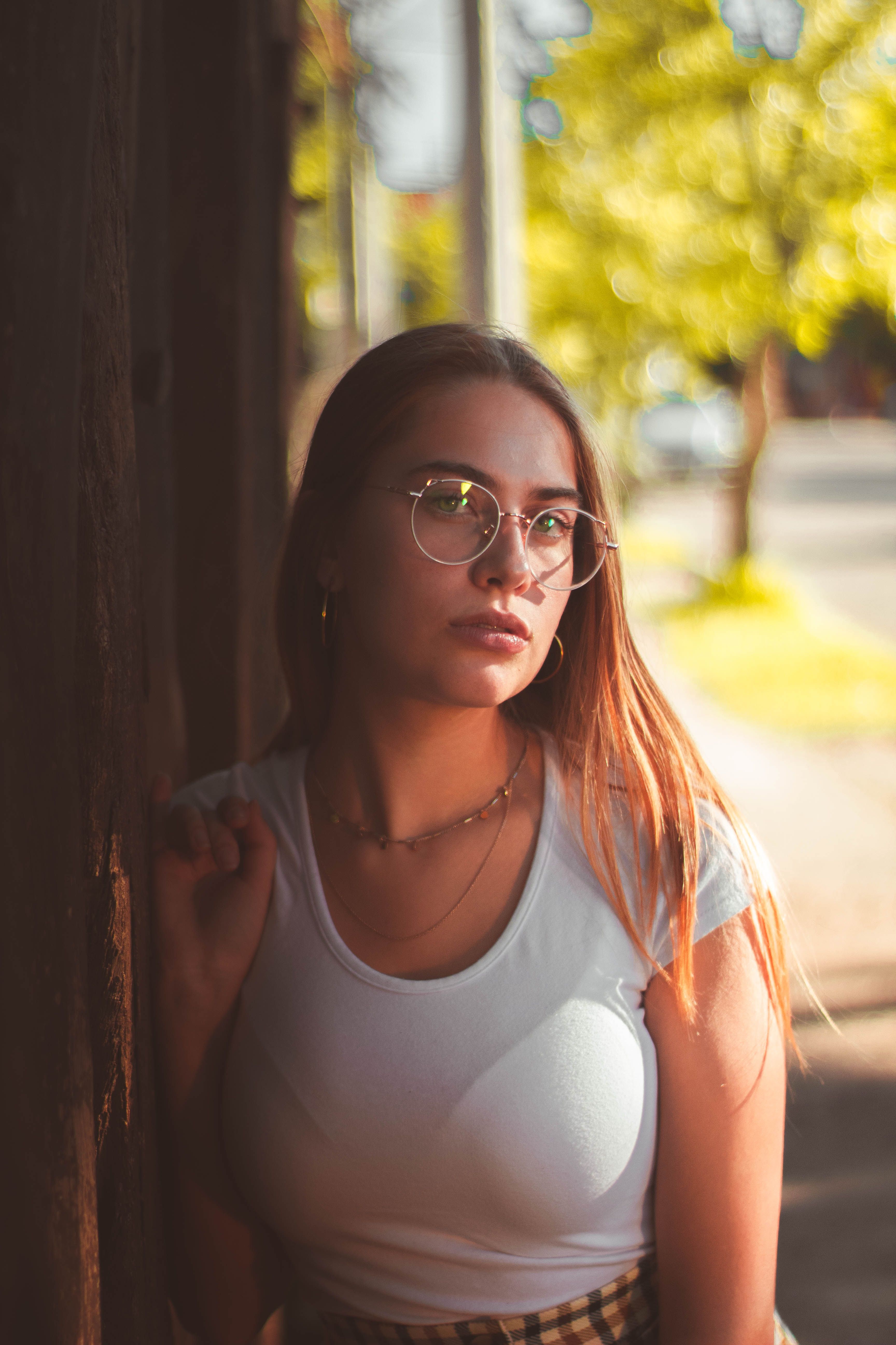 A woman in glasses in a white shirt outside on a sunny day, embodying a relaxed vibe.