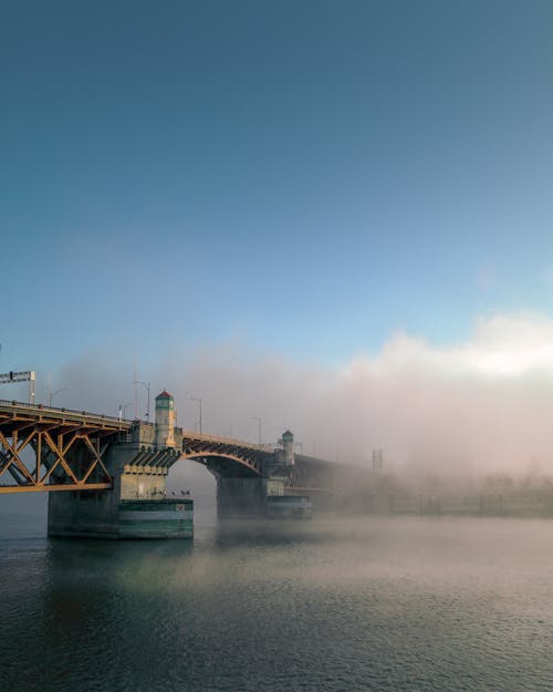 Picturesque cityscape with modern bridge crossing vast rippling river under cloudy blue sky in evening sunlight