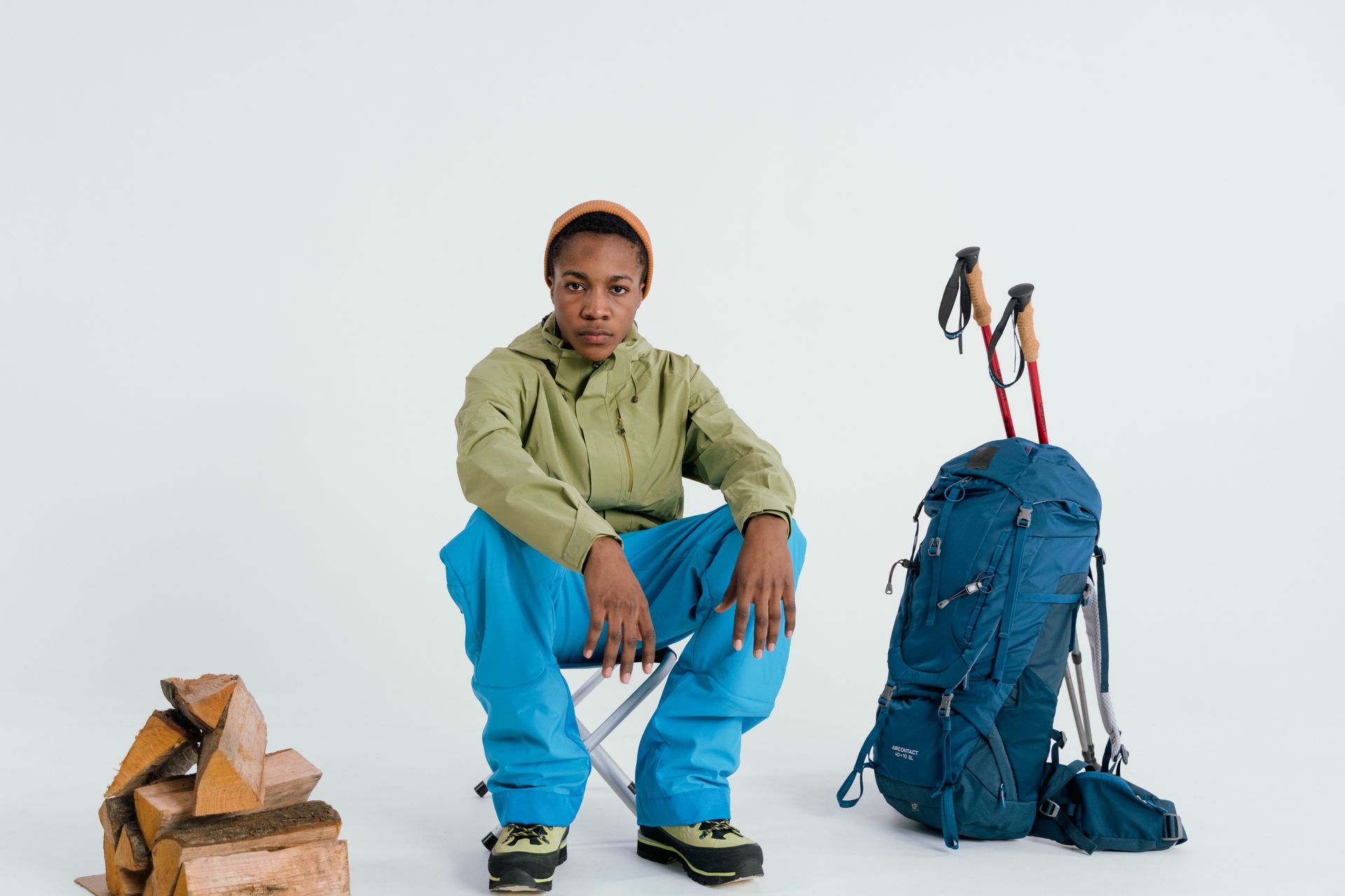Young man sitting with hiking backpack and gear in a studio setting.