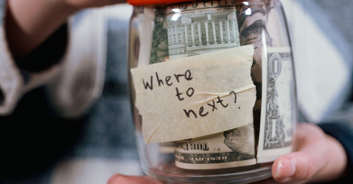 A person holds a savings jar filled with money and a note that says 'Where to next?' symbolizing travel savings.