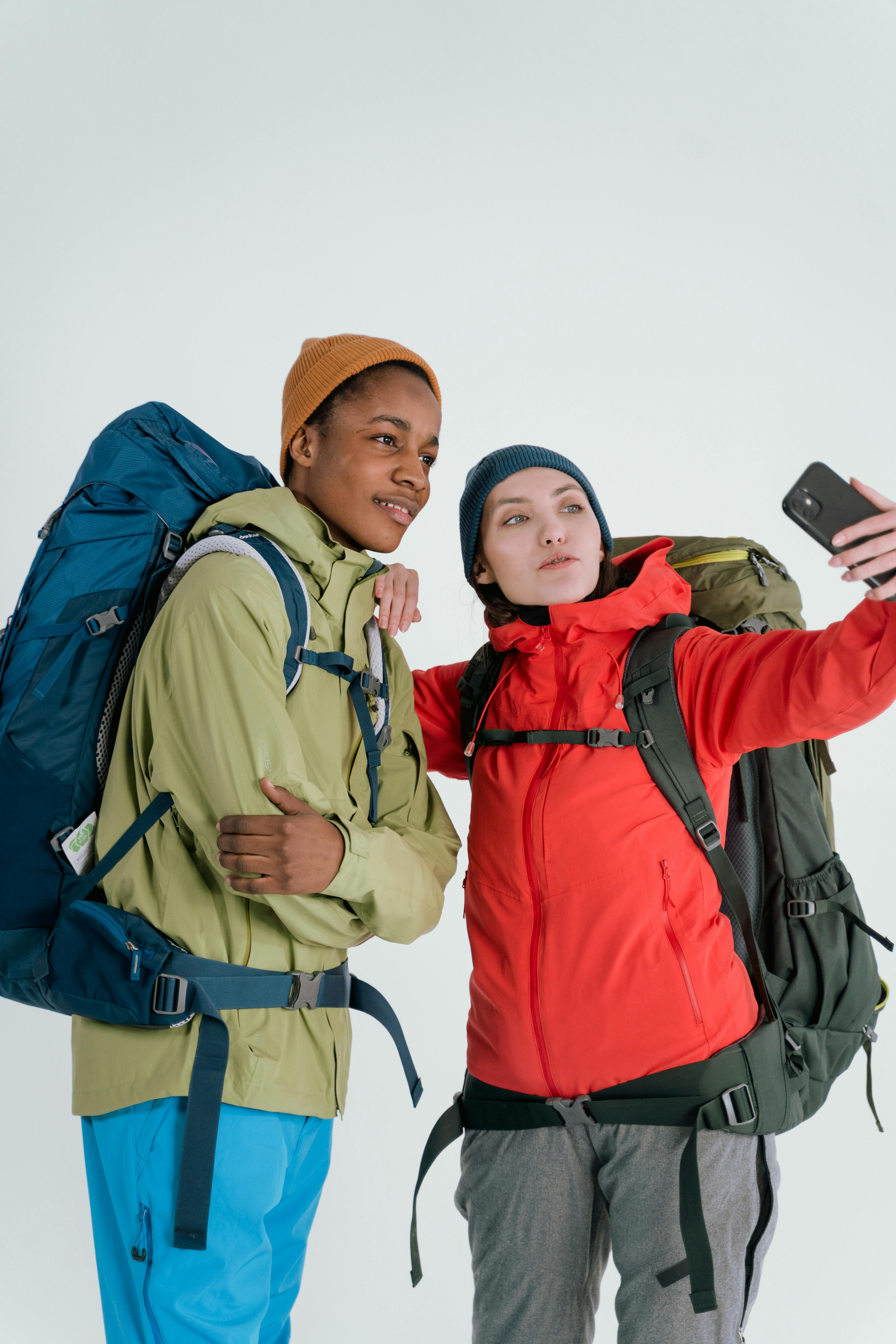 Two diverse hikers take a selfie in a studio setting, capturing their travel adventure.