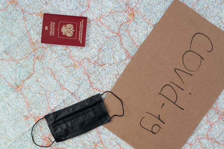 Flat lay of a passport, face mask, and Covid-19 sign on a map, symbolizing travel restrictions.