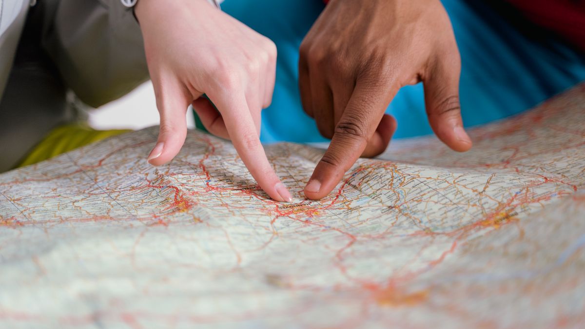 Close-up of diverse hands pointing at a paper map, symbolizing travel planning and navigation.