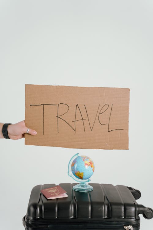 Person Holding Brown Cardboard with Travel Text