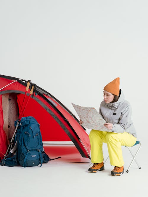 Woman in Gray Jacket and Yellow Pants Sitting beside Red Tent