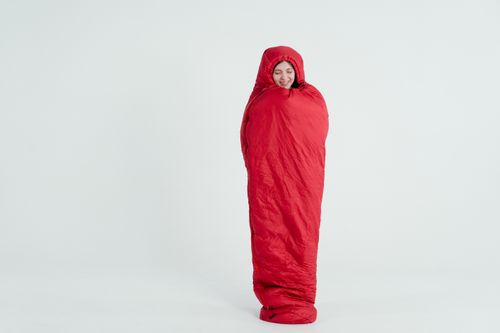 Free A young woman wrapped in a red sleeping bag, smiling with a serene expression. Stock Photo