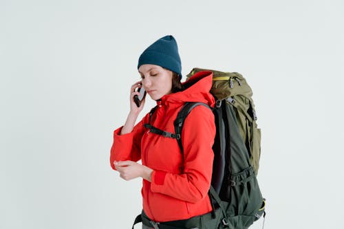 Woman in Red Jacket and Blue Knit Cap using Cellphone