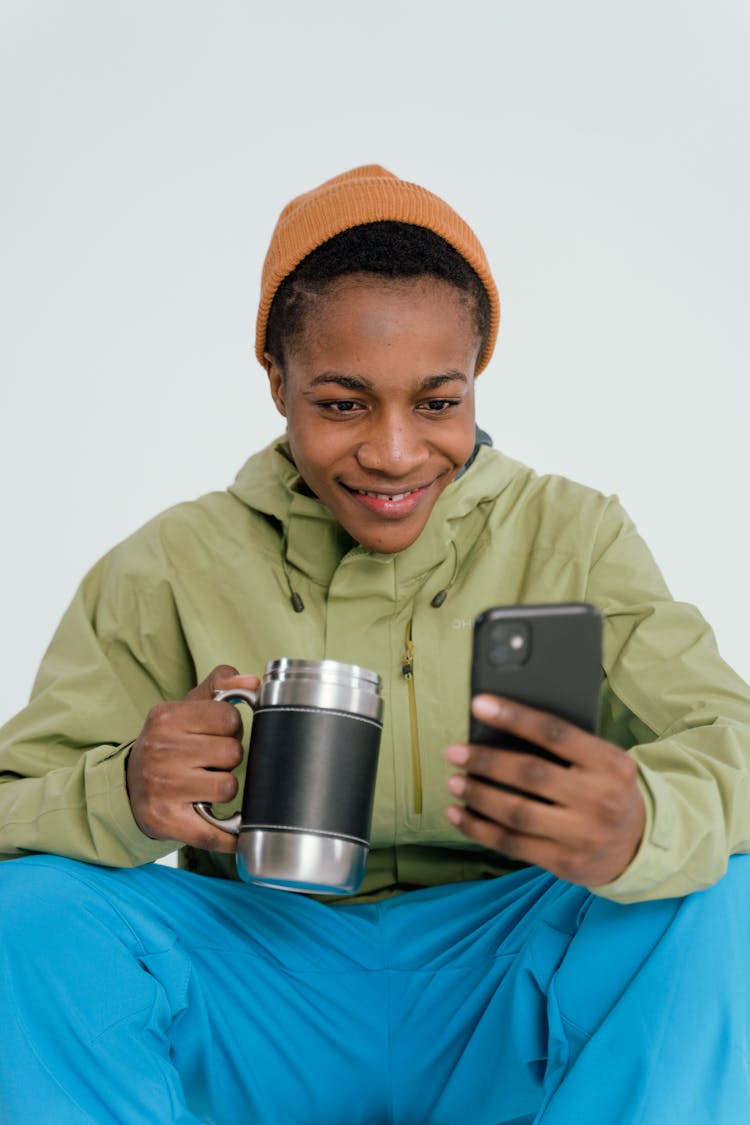 A Man In Green Jacket Holding Silver And Black Thermal Mug