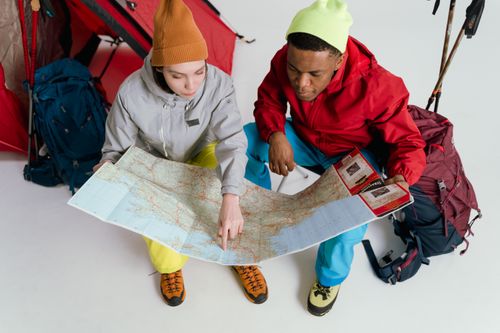Free Two young adventurers studying a map in a studio setting with backpacks, ready for a journey. Stock Photo