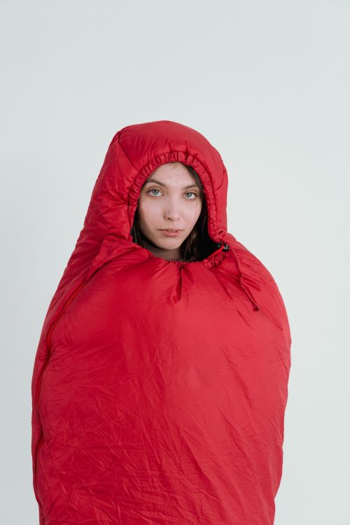 Free A young woman bundled in a red sleeping bag, isolated against a minimalist backdrop. Stock Photo