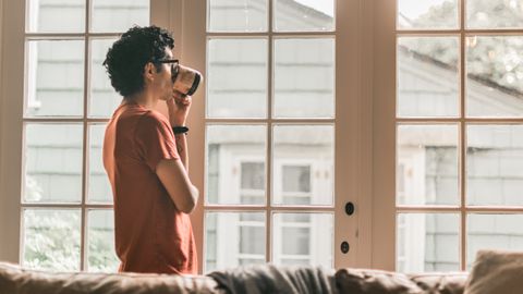 A man with curly hair enjoys a coffee while looking out a bright window, capturing a moment of relaxation.