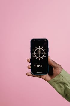 Close-up of a hand holding a smartphone with a compass app against a pink background