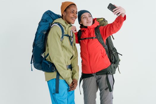 Two friends taking a selfie during a winter hiking adventure, wearing colorful outdoor gear and backpacks.