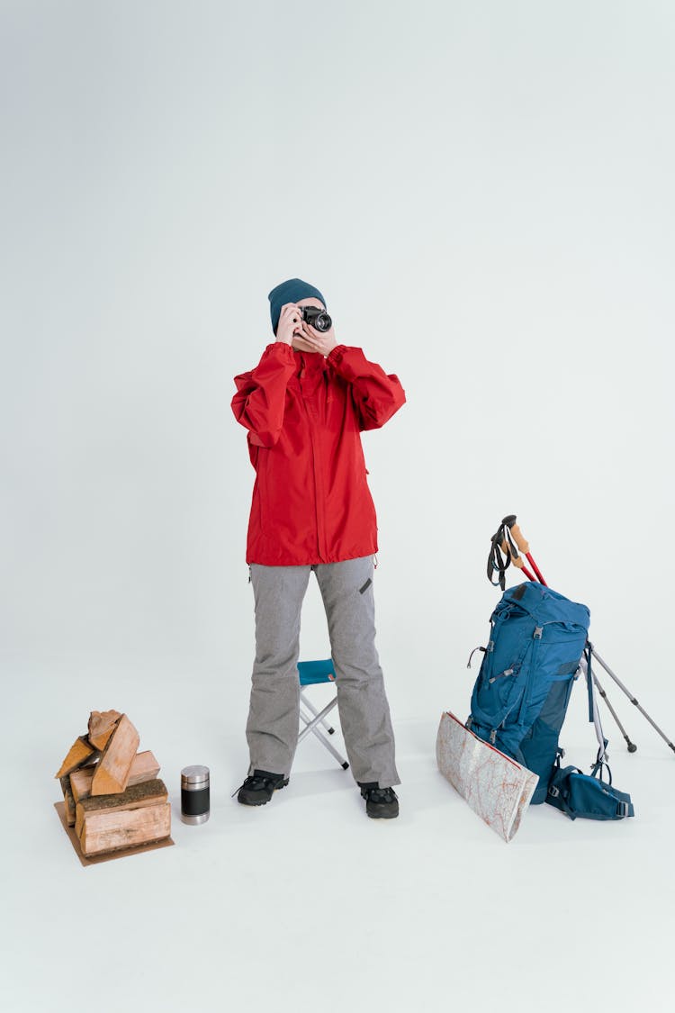 Person In Red Jacket With Packed Bags Looking Through A Camera