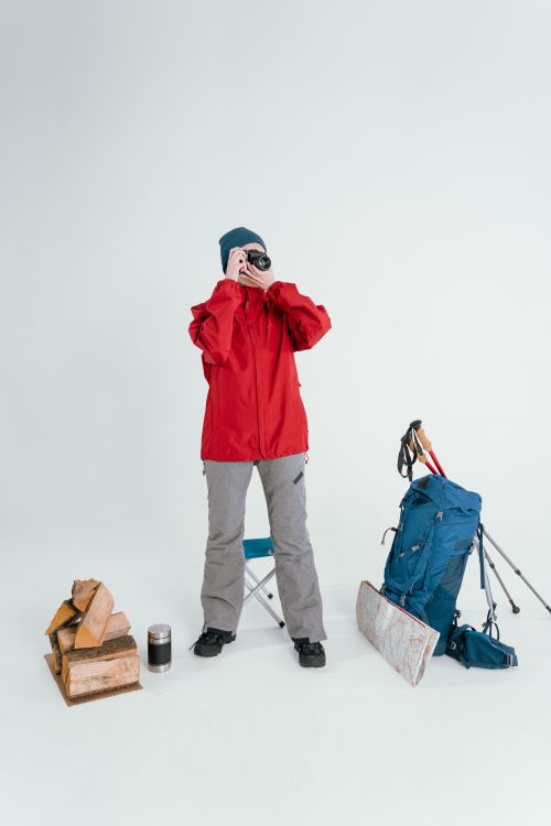 Free Woman in winter clothing preparing for hiking with backpack and camera, standing indoors. Stock Photo