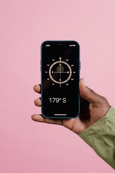 Close-up of a hand holding a smartphone displaying a compass app against a pink background.
