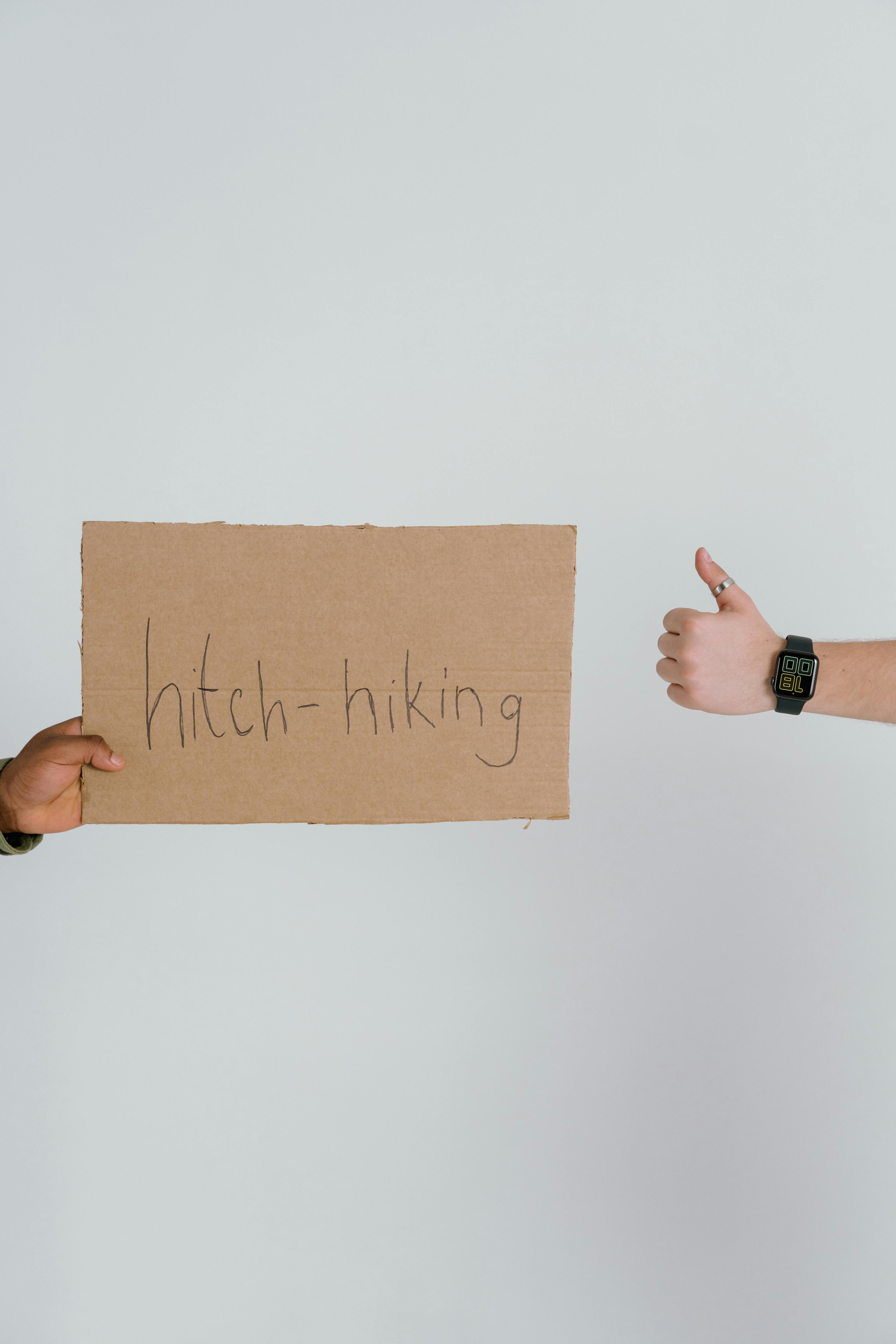 person holding a hitchhiking sign and a person making hand gesture