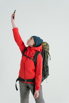 A hiker wearing a red jacket and backpack uses a smartphone. Outdoor winter adventure.