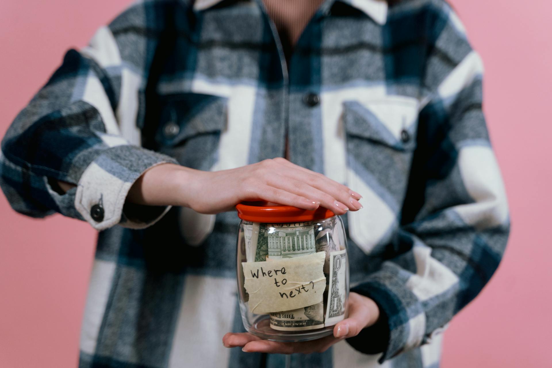 Woman in plaid shirt holds money jar with travel goals in mind.