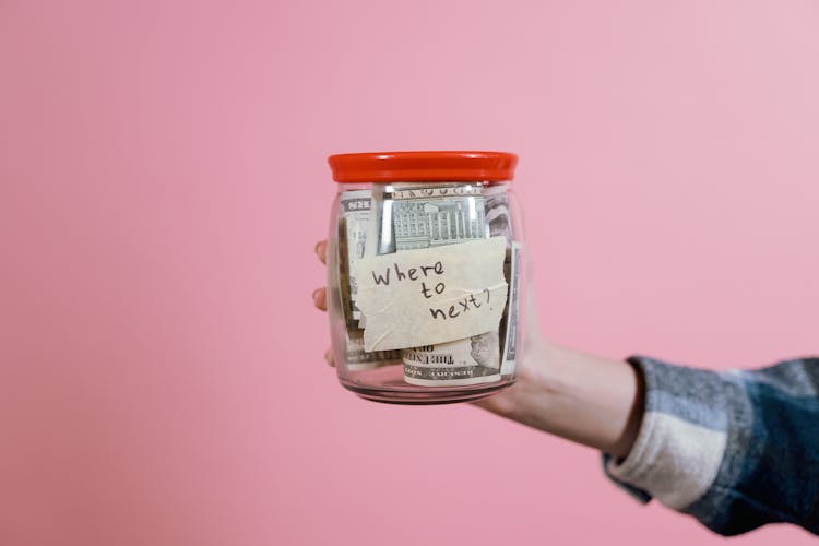 A Person Holding A Glass Jar With Money