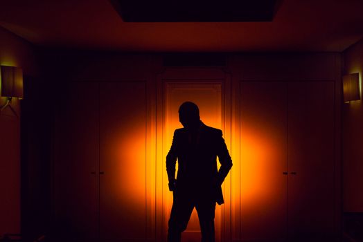 Silhouetted man stands in dark room with warm backlighting, showcasing mystery and intrigue.